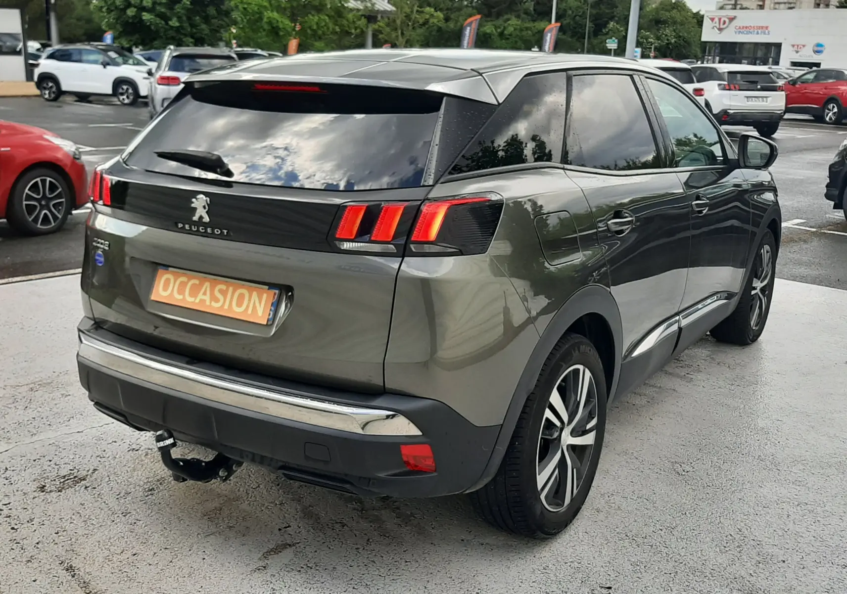 Vue 3/4 arrière droite d’un Peugeot 3008 gris amazonite avec feux arrière LED et attelage visible sur parking.