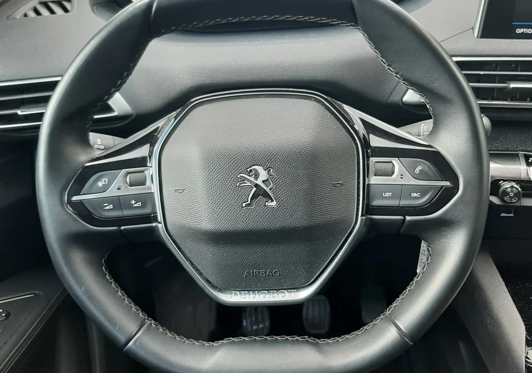 Vue rapprochée du volant noir du Peugeot 3008 2019, avec commandes intégrées et tableau de bord numérique en arrière-plan.