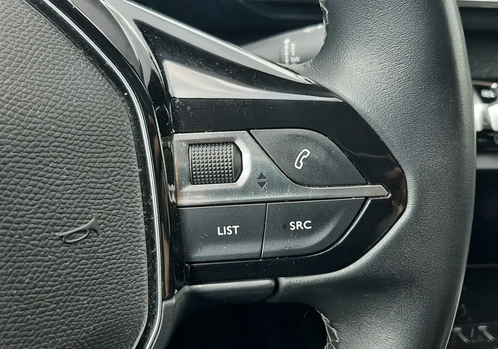 Gros plan sur les commandes gauche du volant noir en cuir du Peugeot 3008 gris Amazonite, boutons LIST et SRC visibles.