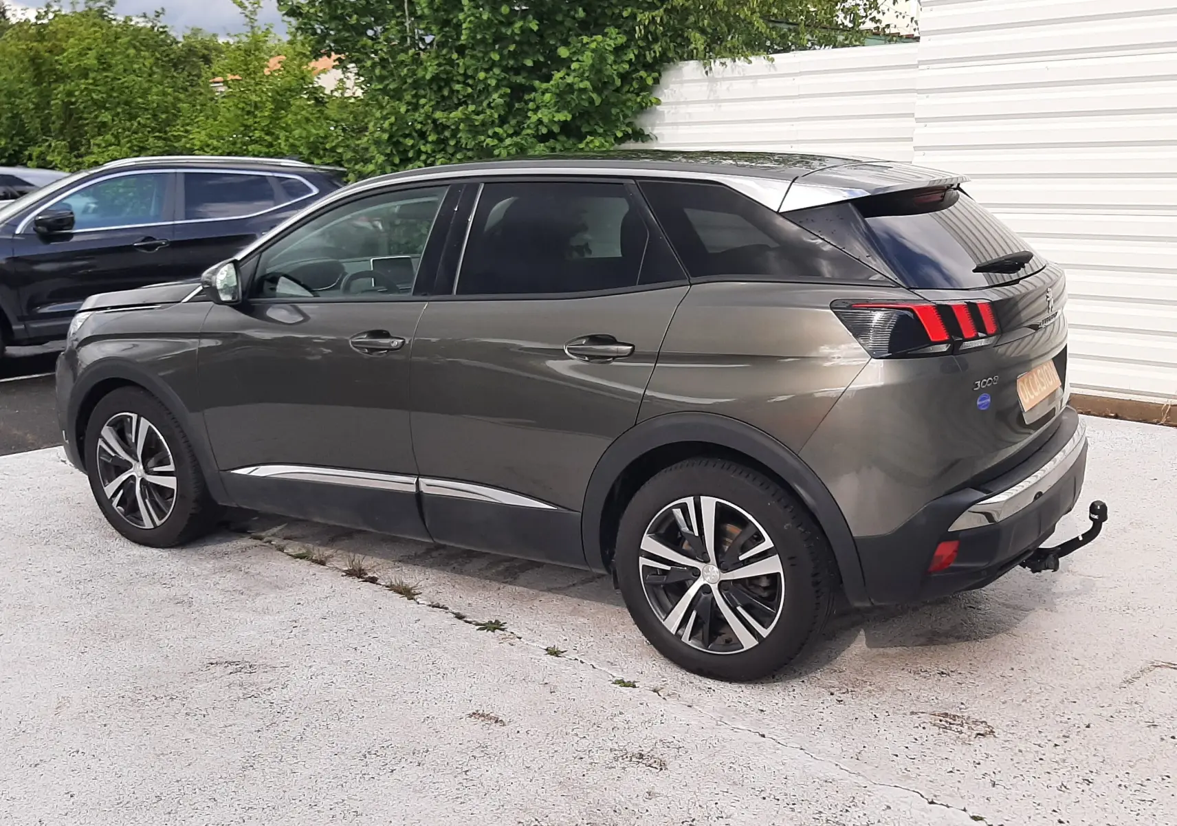 Peugeot 3008 gris amazonite vue 3/4 arrière droit, avec barres de toit noires et attelage visible.
