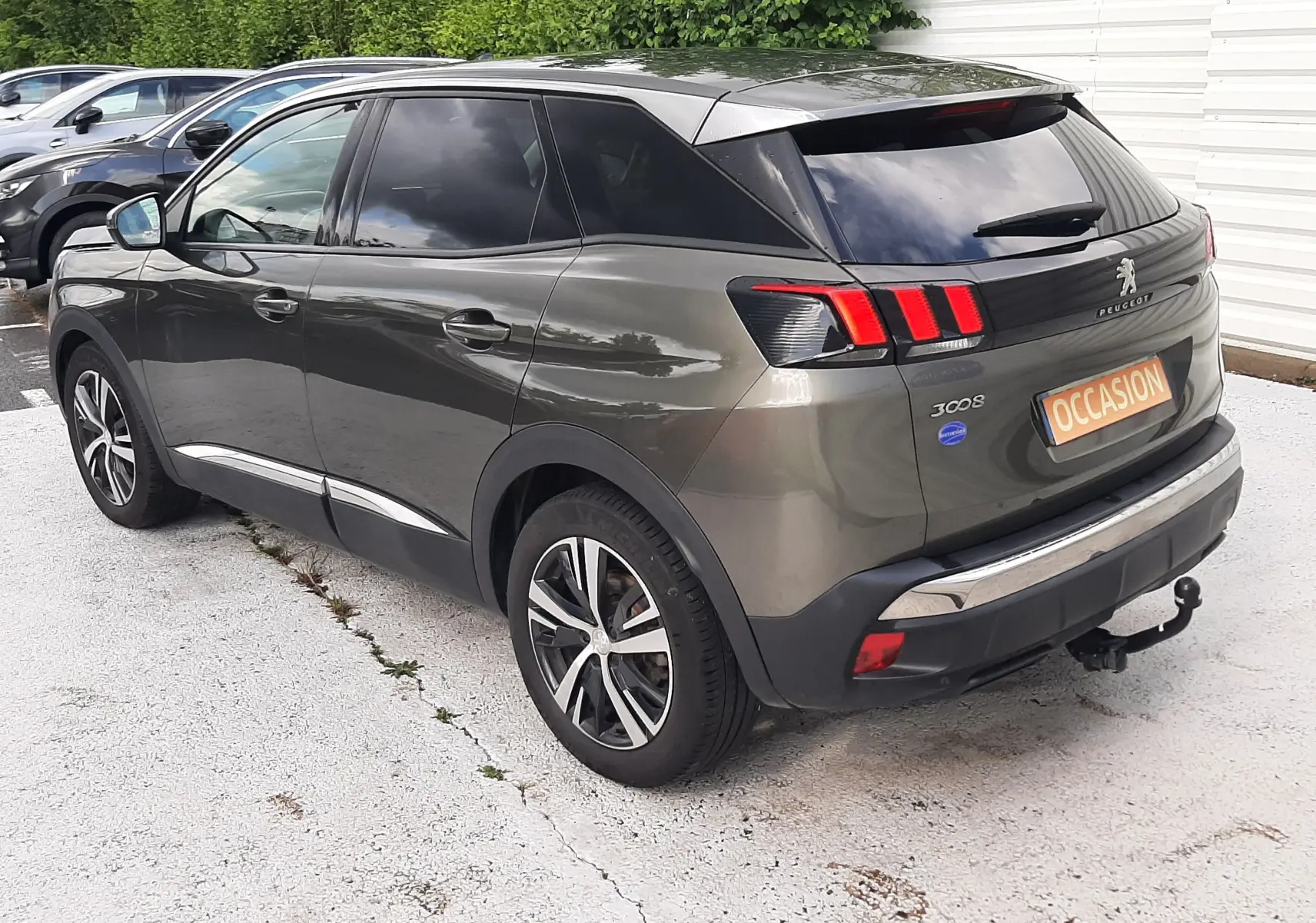 Peugeot 3008 gris amazonite vue 3/4 arrière droit, feux arrière à effet griffes et attelage visible.