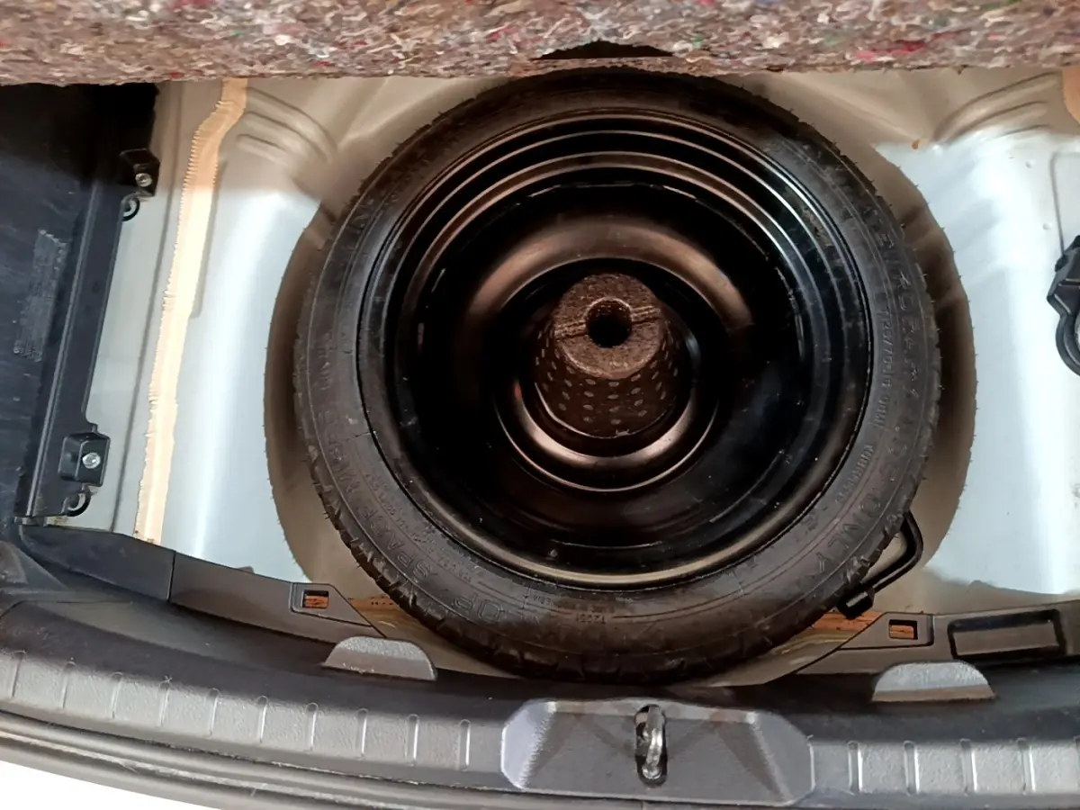 Vue plongeante sur la roue de secours noire logée dans le coffre blanc d'une Toyota Yaris blanche.