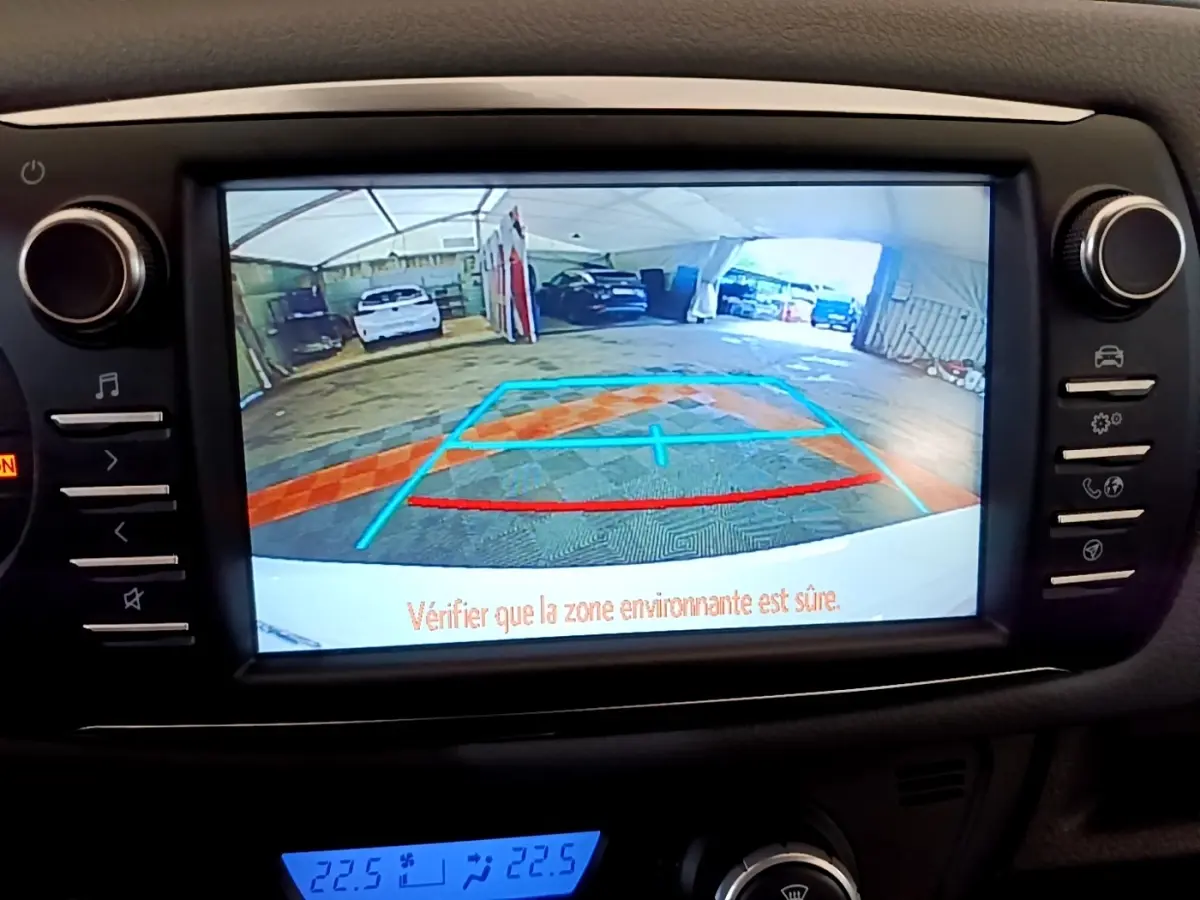 Écran tactile central montrant la caméra de recul d'une Toyota Yaris blanche dans un garage, avec repères de stationnement.