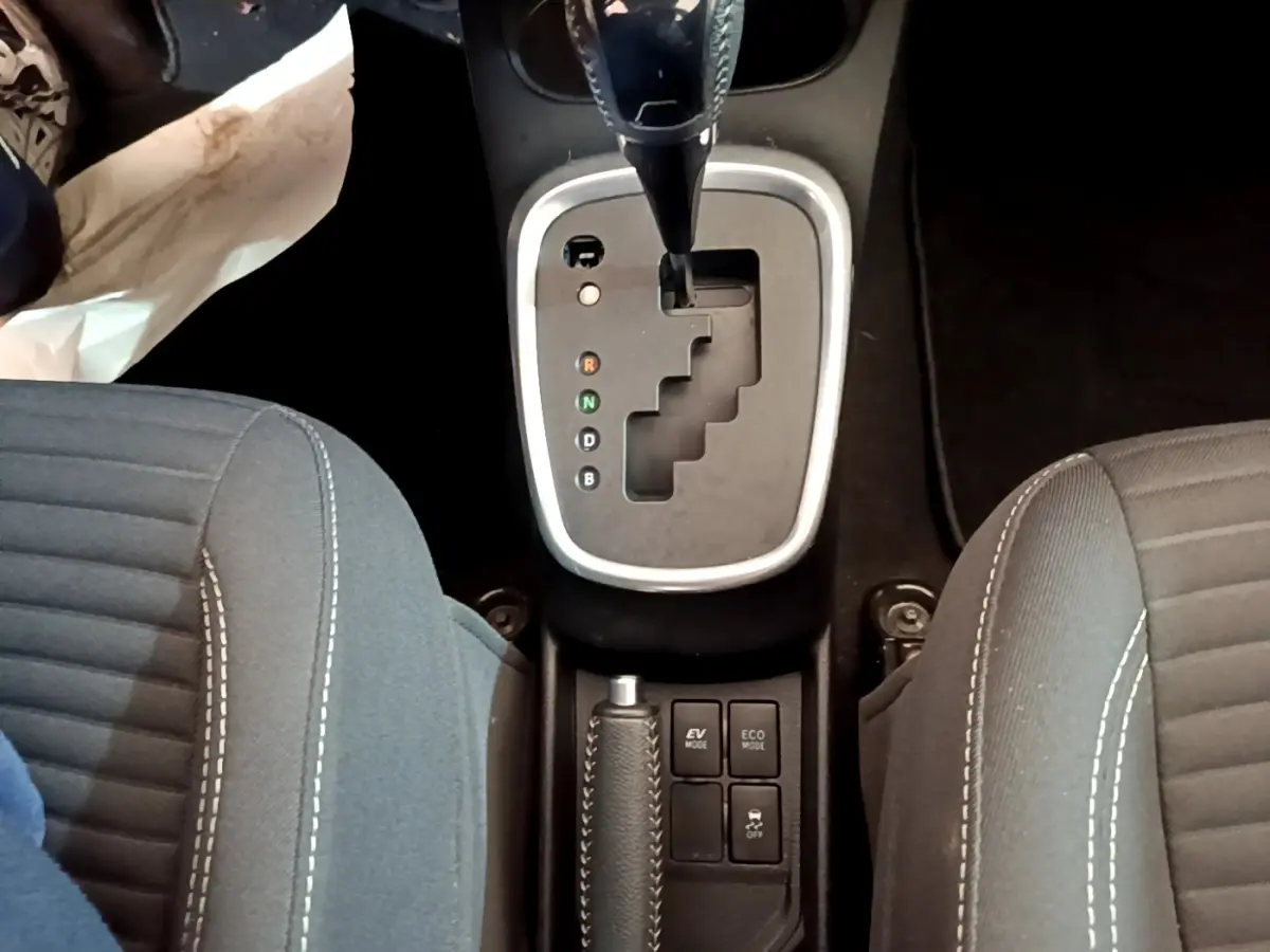 Vue plongeante sur la console centrale de la Toyota Yaris hybride 2019, montrant la boîte auto et les sièges tissu gris.