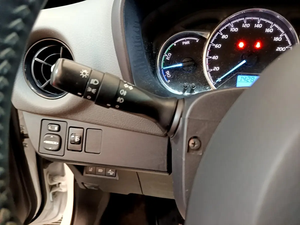 Vue rapprochée du tableau de bord côté gauche d'une Toyota Yaris blanche, avec commandes des phares et compteurs éclairés.