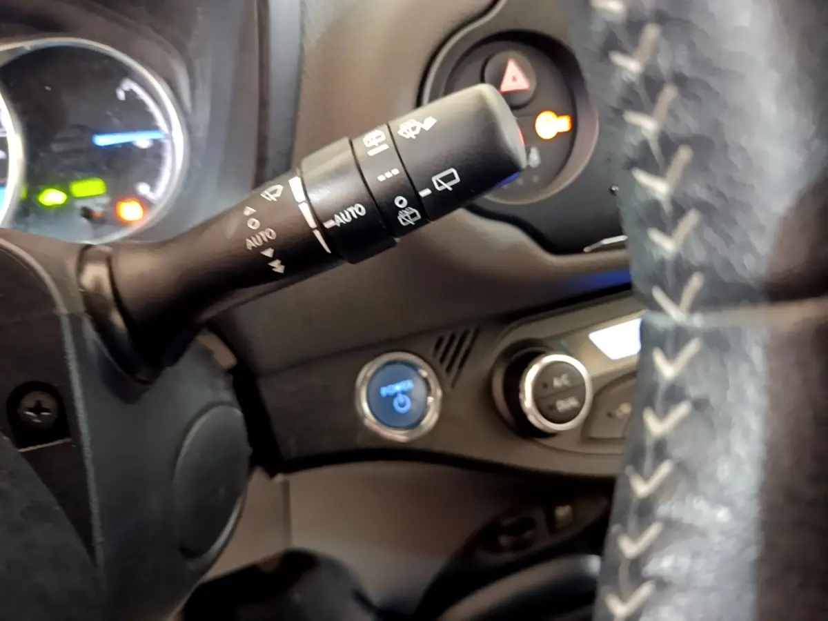 Gros plan intérieur sur le volant cuir et alu de la Toyota Yaris, avec commandes au volant et bouton start/stop bleu visible.