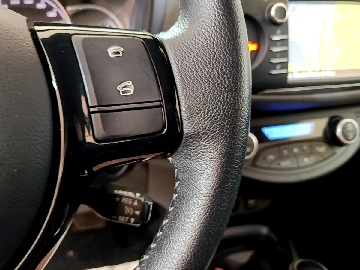 Gros plan sur le volant cuir et alu de la Toyota Yaris blanche avec commandes multifonctions et écran tactile en arrière-plan.