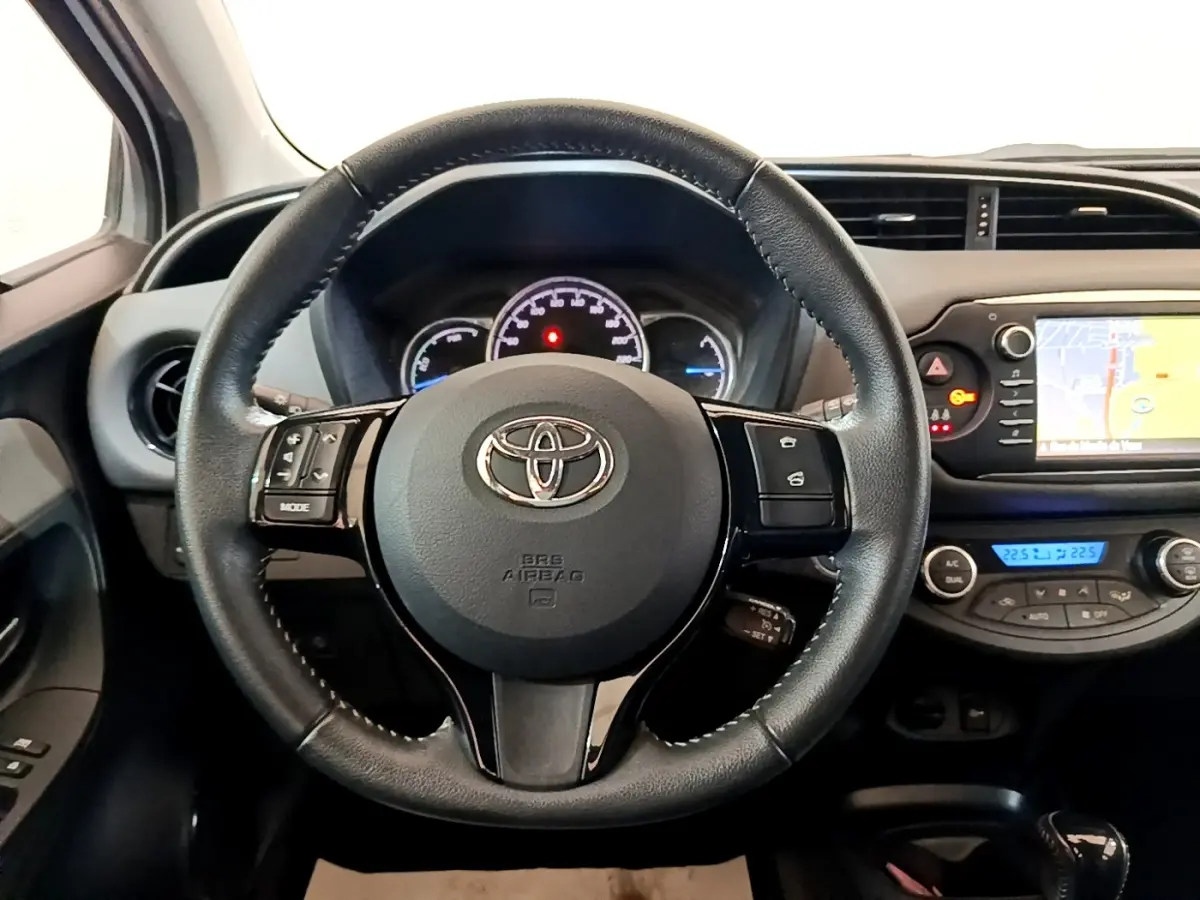 Vue intérieure centrée sur le volant cuir et alu de la Toyota Yaris blanche, avec tableau de bord et écran tactile visible.
