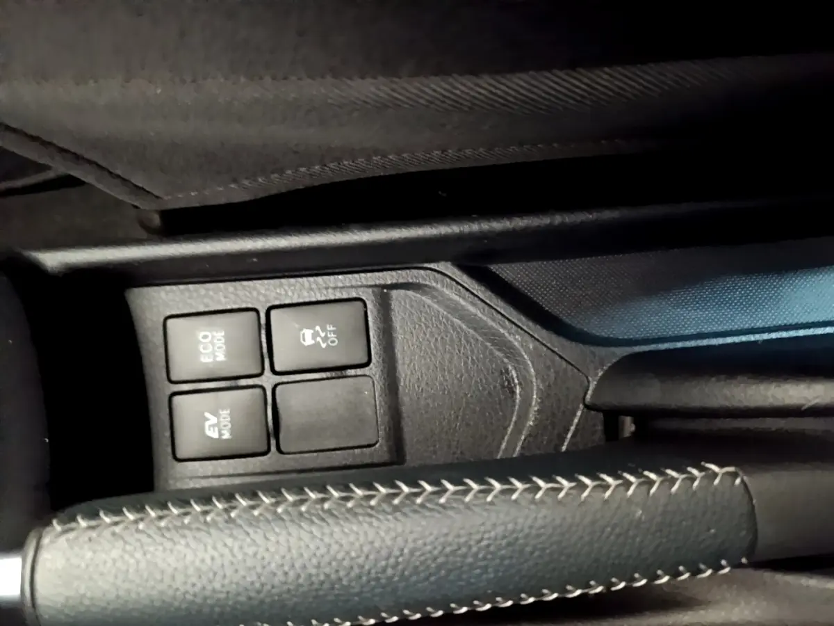 Gros plan sur le frein à main en cuir noir avec surpiqûres blanches et les boutons de modes de conduite d'une Toyota Yaris blanche.
