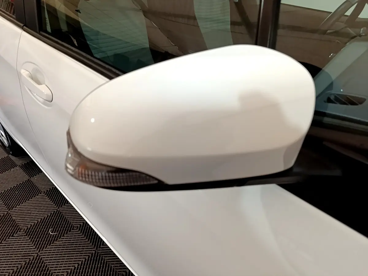 Gros plan sur le rétroviseur côté gauche blanc d'une Toyota Yaris hybride 2019, avec la portière visible en arrière-plan.