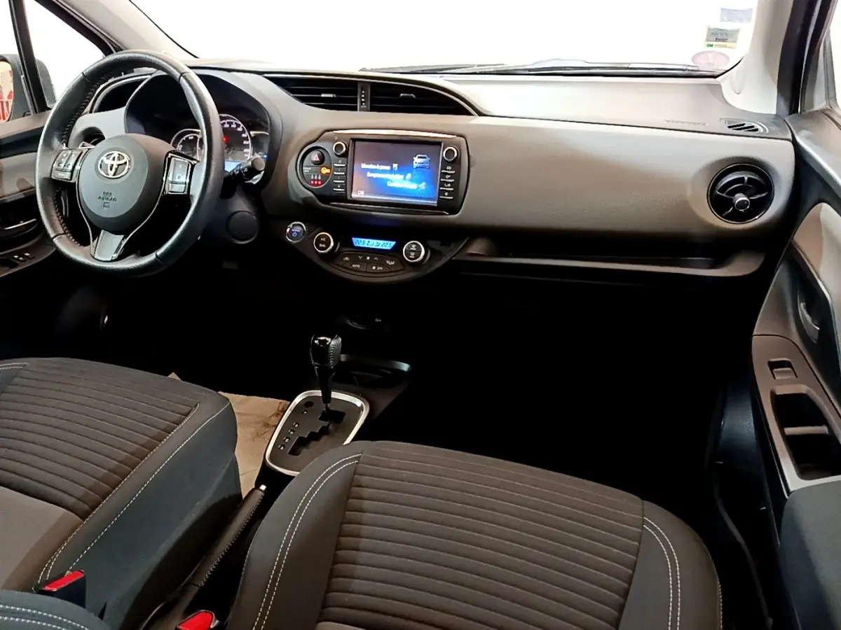 Vue intérieure avant droite de la Toyota Yaris 2019, volant cuir multifonctions et écran tactile central allumé.