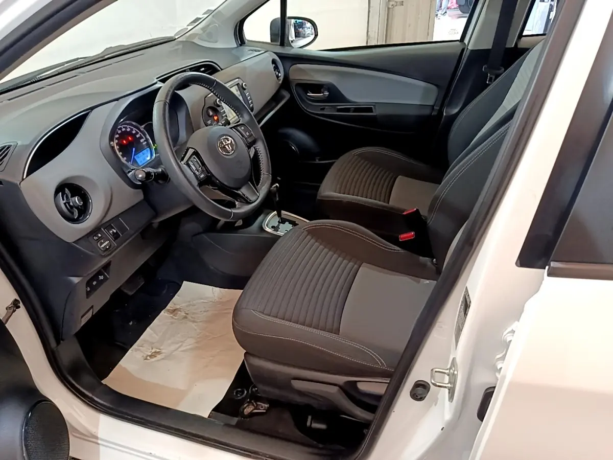 Vue intérieure côté conducteur de la Toyota Yaris blanche 2019, volant multifonctions en cuir et tableau de bord visible.