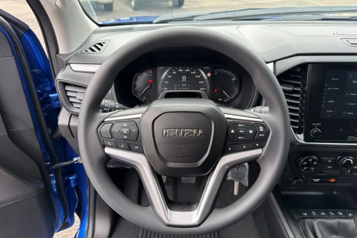 Vue centrée sur le volant multifonctions d’un Isuzu D-MAX bleu Biarritz, avec tableau de bord et écran tactile visibles.