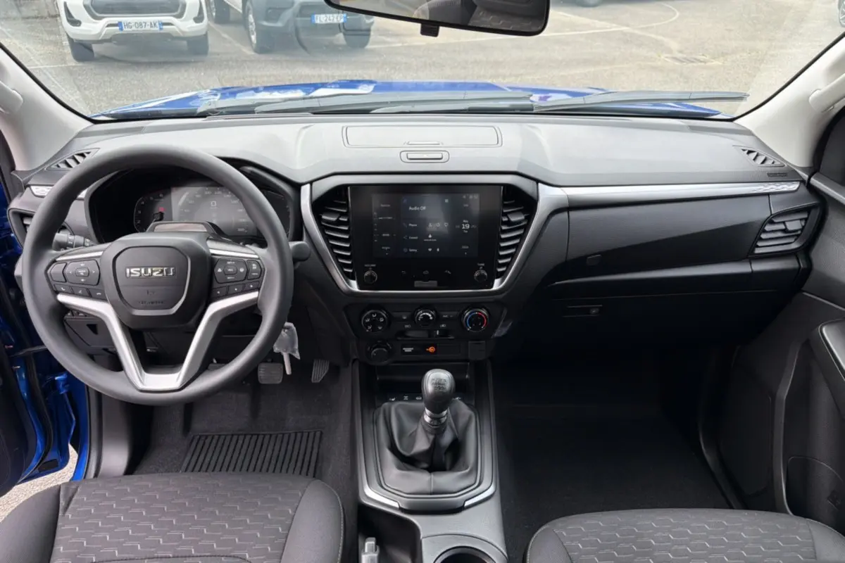 Vue intérieure frontale de l'Isuzu D-MAX bleu Biarritz, montrant le volant multifonctions et la console centrale avec écran tactile.