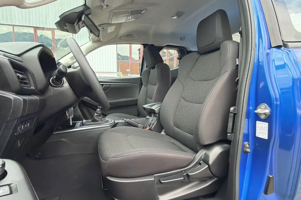 Vue intérieure côté conducteur du pick-up Isuzu D-MAX 2026 bleu Biarritz, sièges tissu et boîte manuelle visible.
