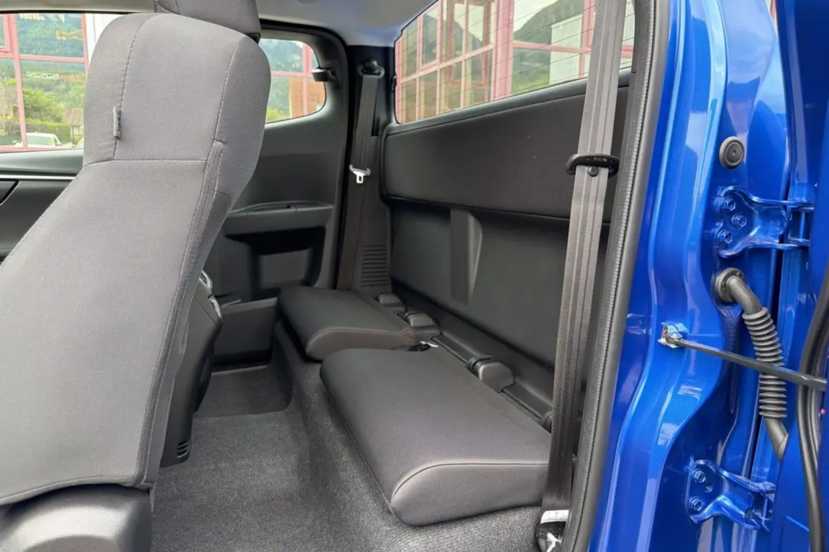 Vue intérieure côté arrière droit du pick-up Isuzu D-MAX bleu Biarritz, montrant les sièges arrière rabattus et la porte ouverte.
