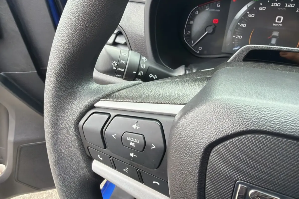 Gros plan sur le volant multifonctions côté gauche de l’Isuzu D-MAX 2026 Biarritz blue metalic, avec commandes audio visibles.