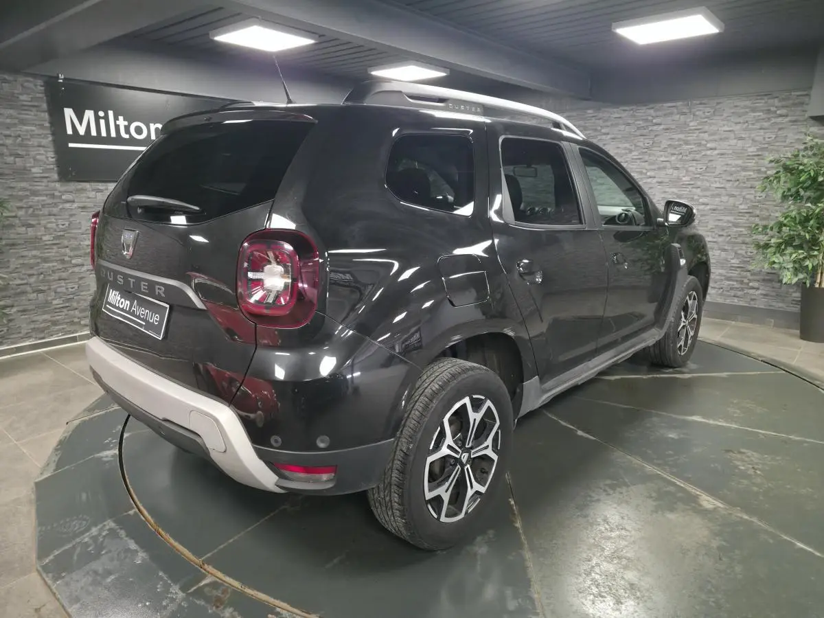 Vue 3/4 arrière droit du Dacia Duster noir nacré avec jantes alliage 17 pouces et barres de toit argentées.