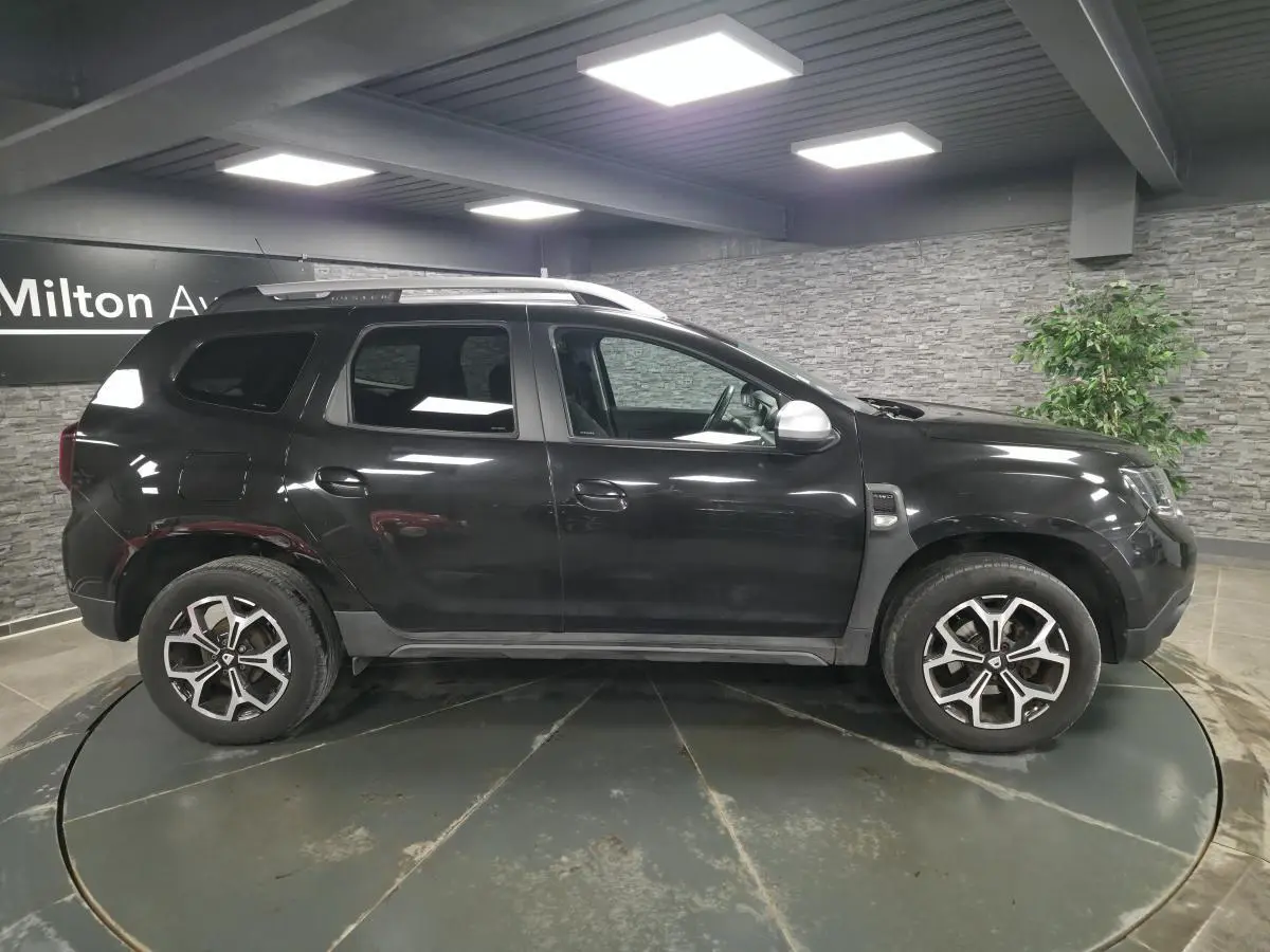Vue de profil côté gauche d'un Dacia Duster noir nacré avec jantes alliage 17 pouces dans un showroom.