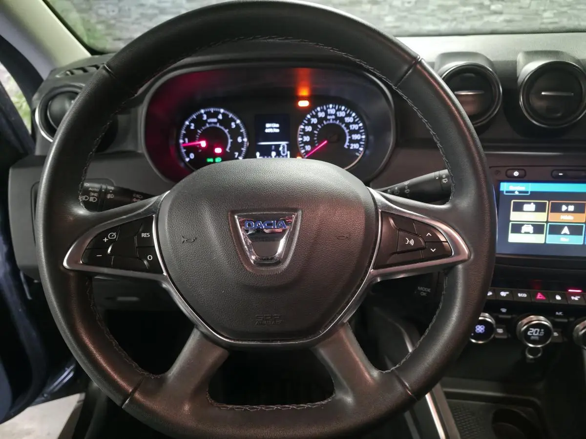 Vue rapprochée du volant noir de Dacia Duster 2019 avec tableau de bord éclairé et écran tactile central visible.