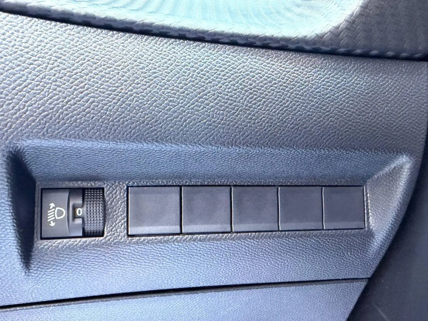 Détail du tableau de bord gris foncé de la Peugeot 208 1.2 100ch, avec commande de réglage des phares.