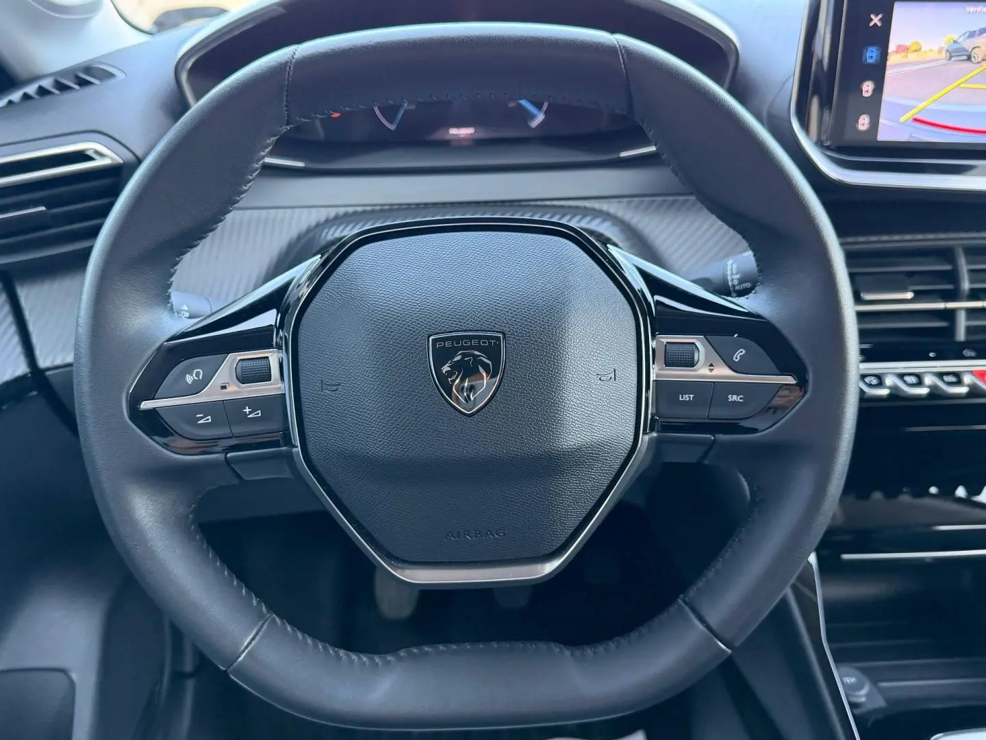 Vue rapprochée du volant cuir noir de la Peugeot 208 2025 avec commandes intégrées et logo lion central.