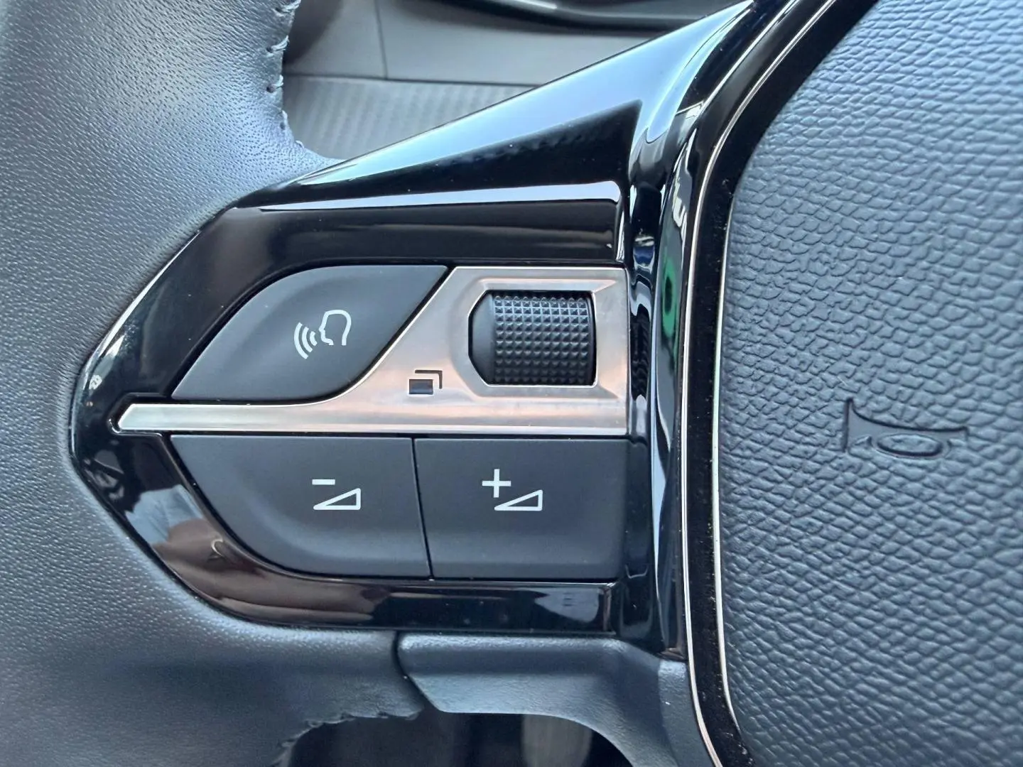Gros plan sur les commandes noires et argentées du volant de la Peugeot 208 gris Selenium, avec bouton molette et réglages audio.