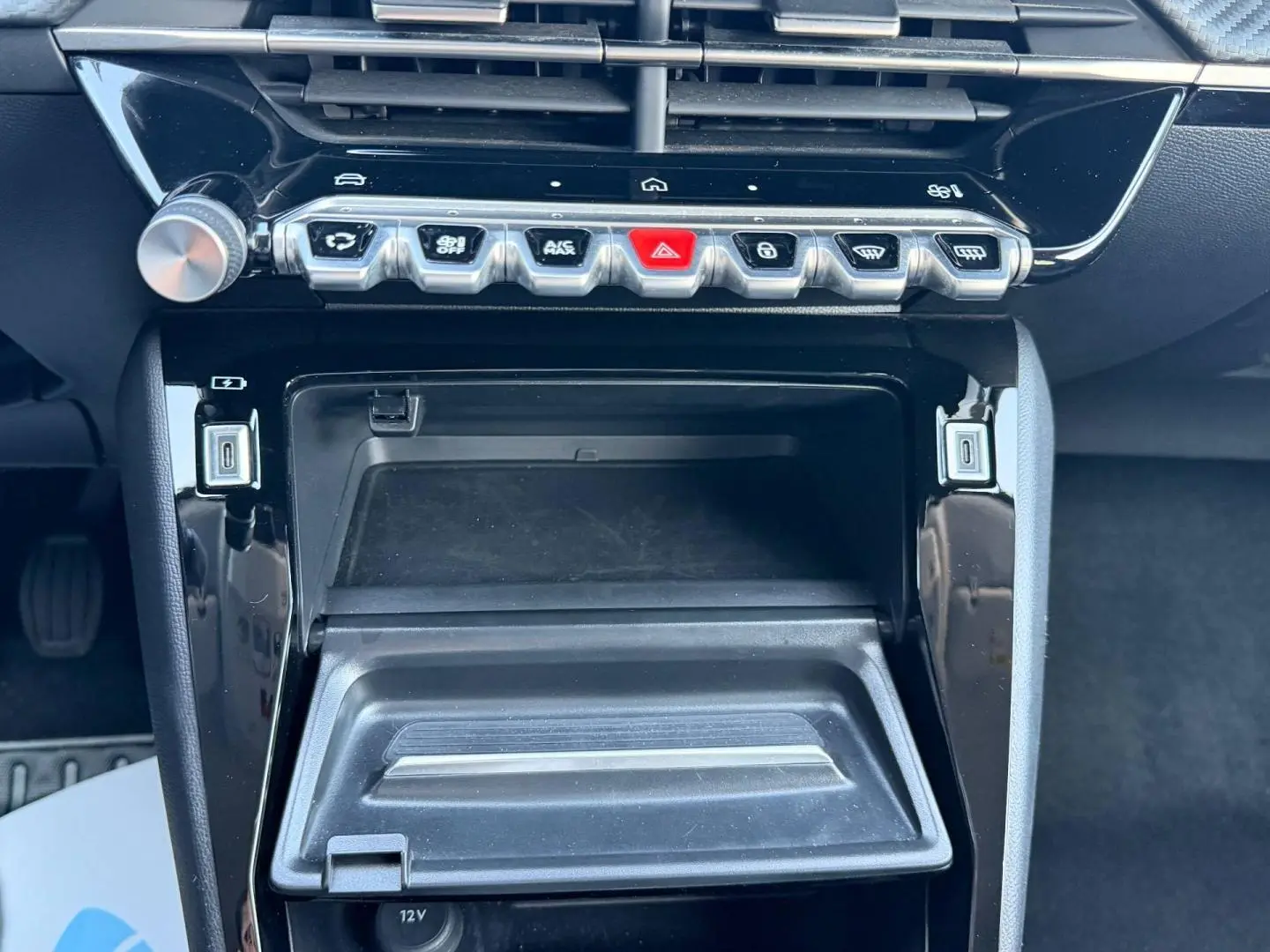 Vue rapprochée de la console centrale noire brillante de la Peugeot 208 2025 avec boutons de commande et prise USB.