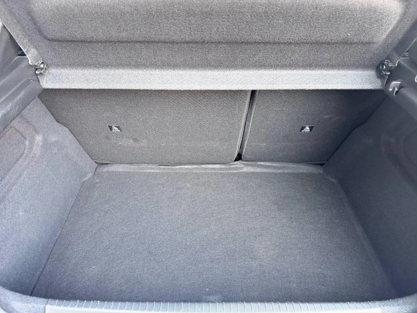 Coffre ouvert de la Peugeot 208 1.2 100ch gris Selenium, montrant l'espace de chargement et la banquette arrière rabattable.