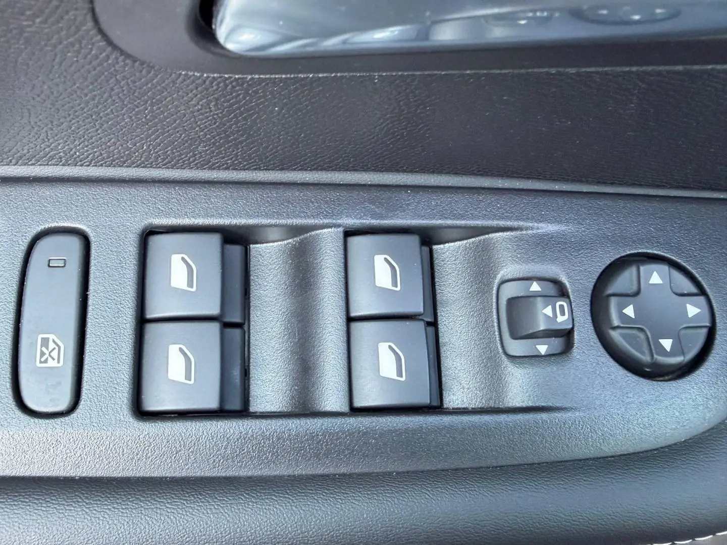 Gros plan sur les commandes de lève-vitres et réglages des rétroviseurs côté conducteur d'une Peugeot 208 gris Selenium.