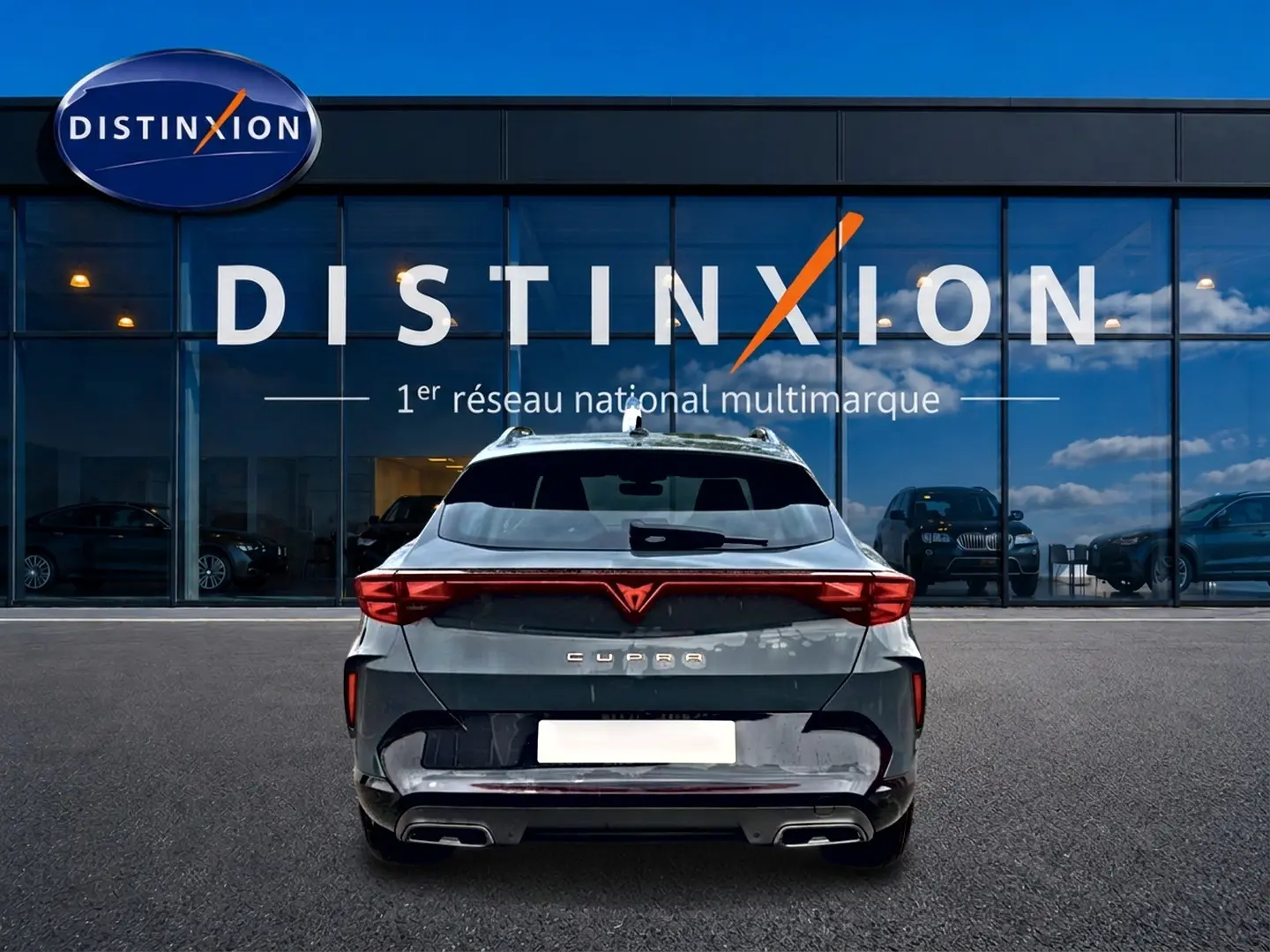 Vue arrière d'un CUPRA Formentor bleu fjord garé devant une vitrine Distinxion, avec feux arrière LED et double sortie d'échappement.