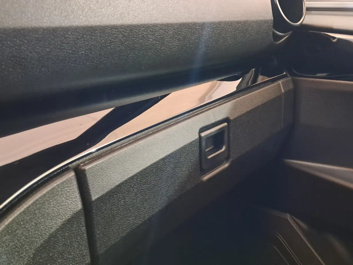 Gros plan sur la boîte à gants noire à ouverture carrée de l'intérieur d'une Aixam Ambition rouge 2025.