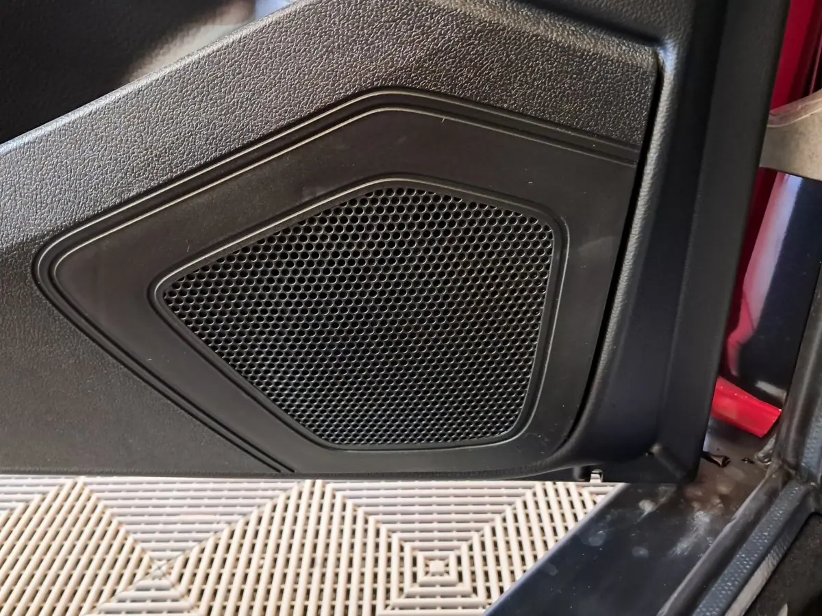 Gros plan sur le haut-parleur noir intégré à la porte côté conducteur d'une Aixam Ambition rouge 2025.