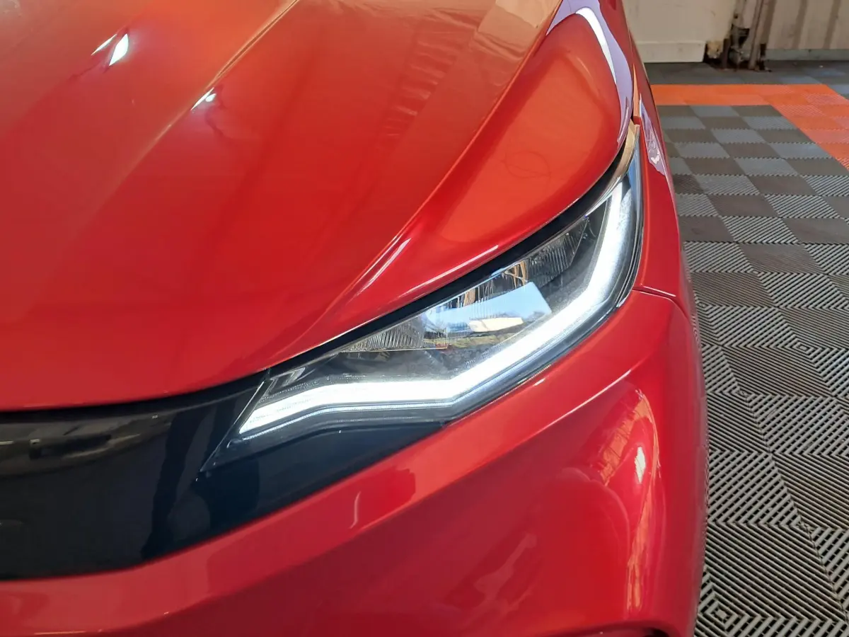 Gros plan sur le phare avant droit d'une AIXAM AMBITION rouge 2025 avec éclairage LED et carrosserie brillante.