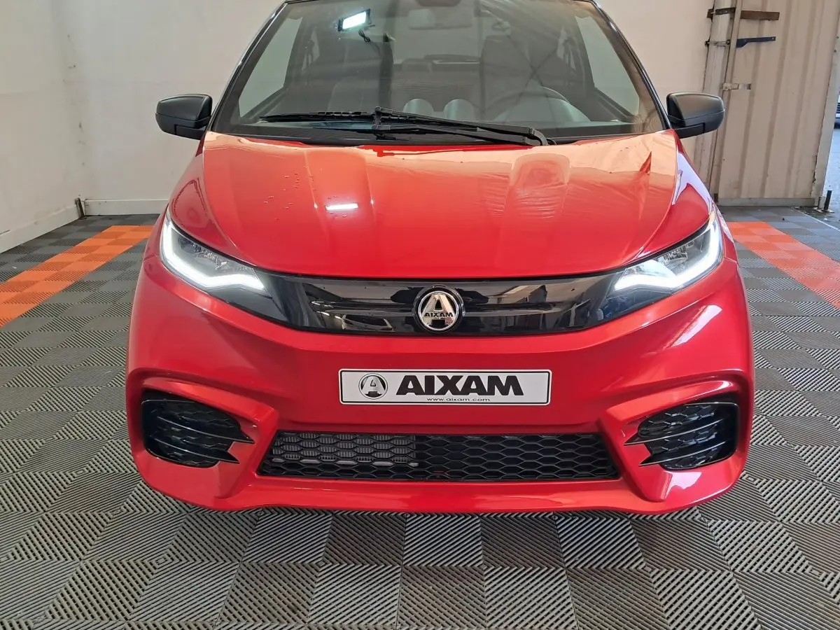Vue frontale d'une Aixam Ambition rouge 2025 avec phares allumés et calandre noire brillante.