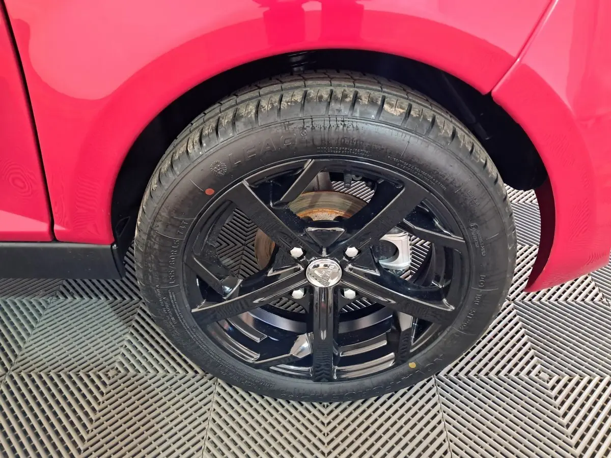 Gros plan sur la roue avant droite noire d'une Aixam Ambition rouge, mettant en valeur la jante sportive brillante.