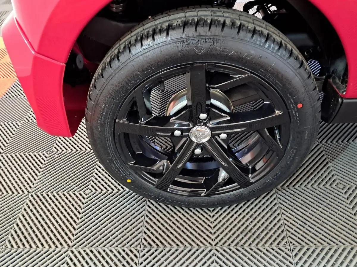 Gros plan sur la roue avant gauche noire brillante d'une Aixam Ambition rouge, soulignant la jante sportive cinq branches.