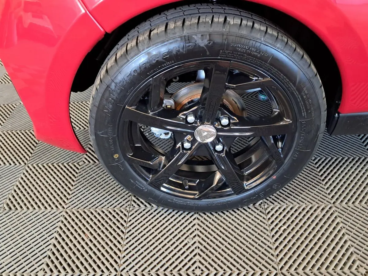 Gros plan sur la roue avant gauche noire brillante d'une Aixam Ambition rouge 2025 avec disque de frein visible.