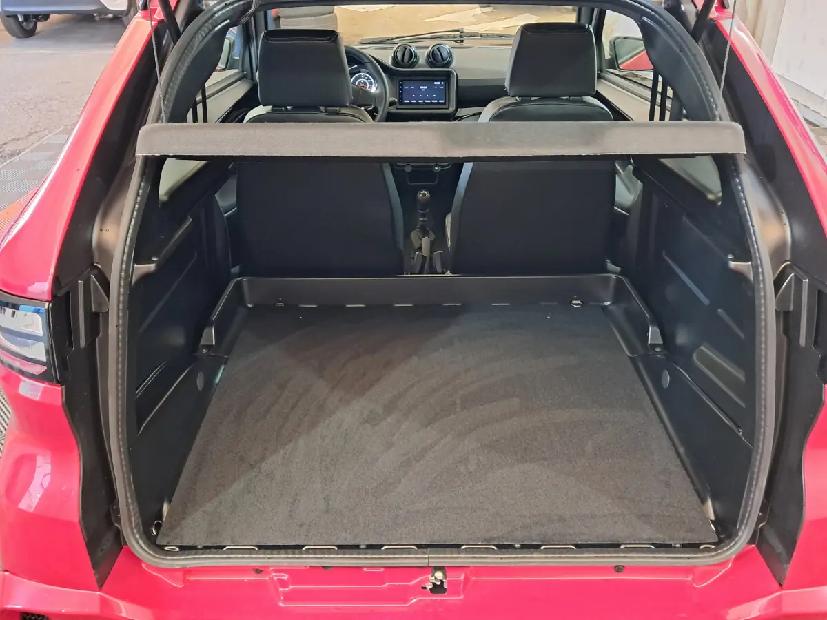 Vue arrière ouverte du coffre d'une Aixam Ambition rouge 2025, montrant l'intérieur spacieux et les sièges avant noirs.