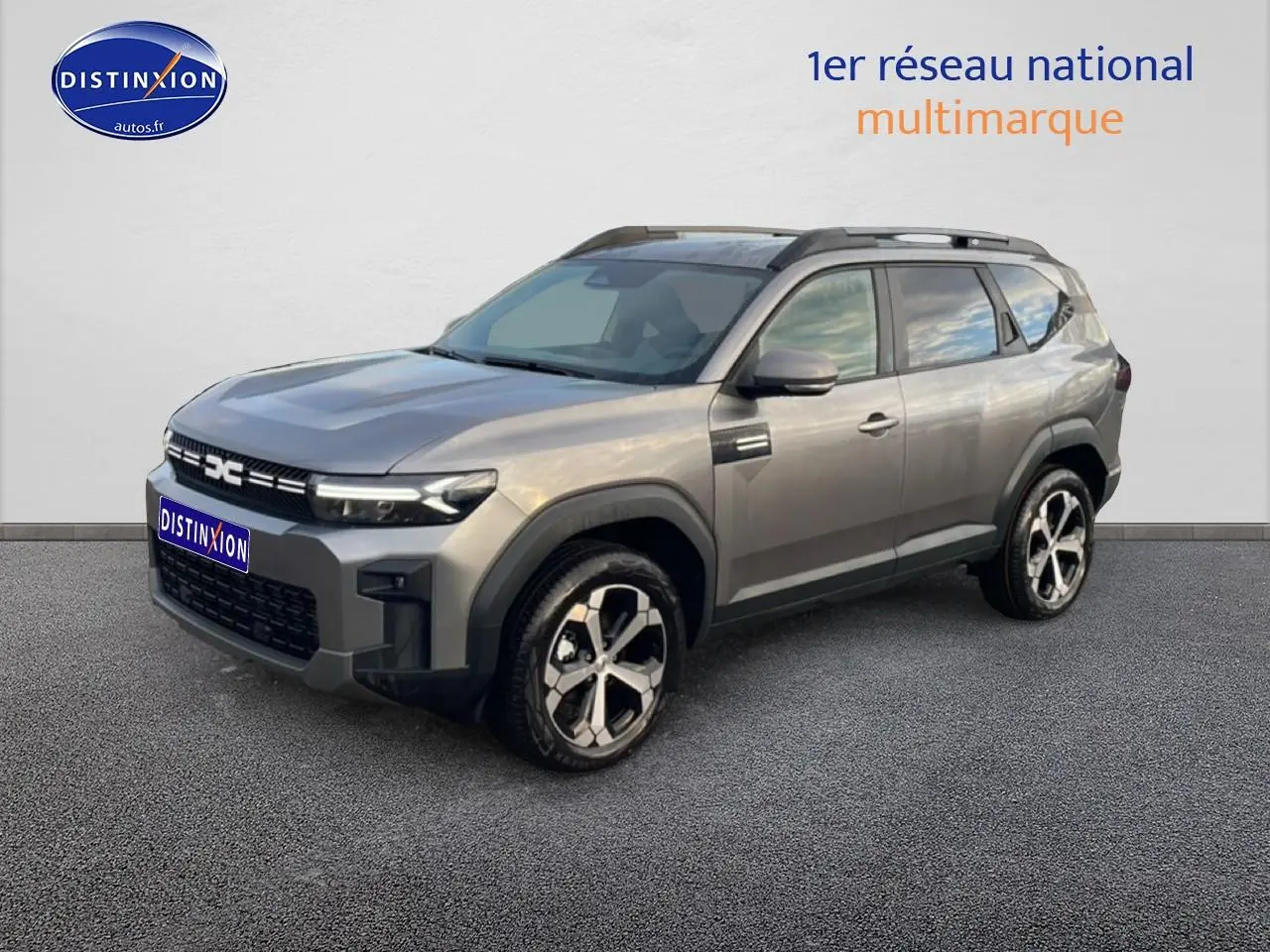 SUV Dacia Bigster gris schiste en 3/4 avant droit, avec jantes alliage diamantées et barres de toit noires.