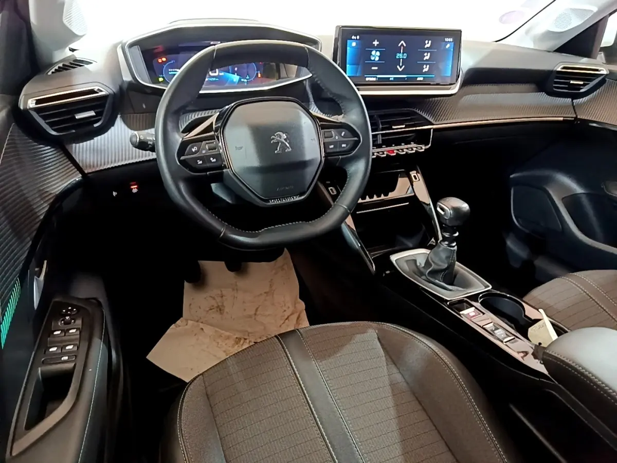 Vue intérieure avant de la Peugeot 208 PureTech 100, tableau de bord noir avec écran tactile et volant cuir multifonctions.