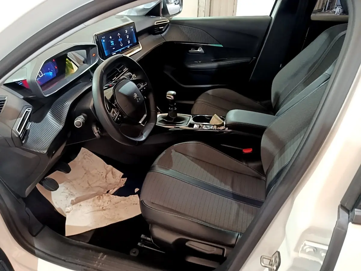 Vue intérieure côté conducteur de la Peugeot 208 blanche, montrant le volant cuir, tableau de bord digital et écran tactile central.