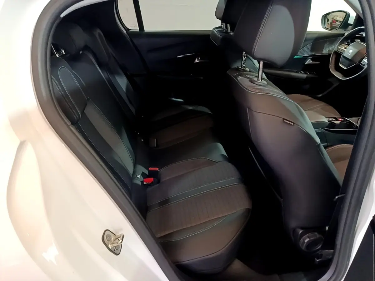 Vue intérieure côté gauche arrière de la Peugeot 208 blanche, montrant les sièges noirs et le volant multifonctions.