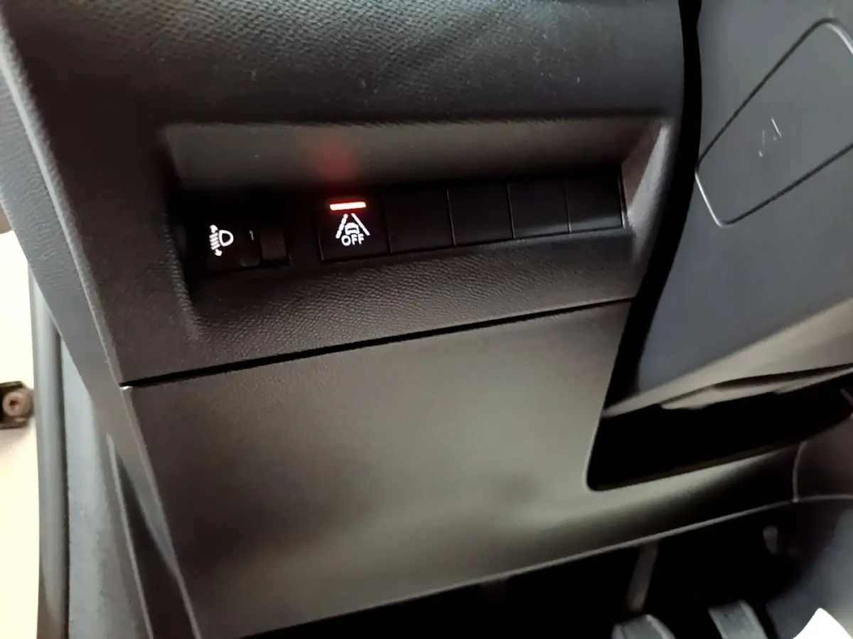 Gros plan sur les commandes noires sous le tableau de bord d'une Peugeot 208 blanche, avec témoin d'alerte allumé.