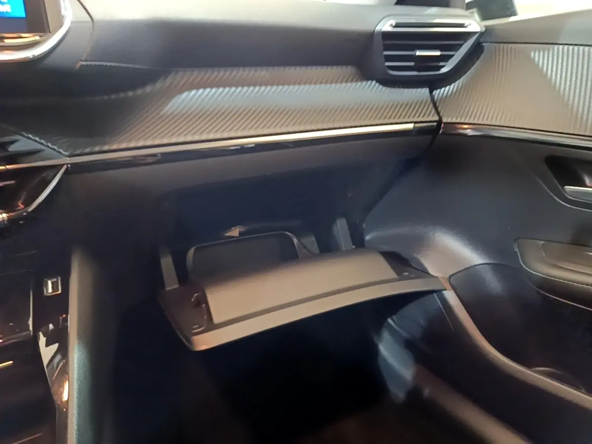 Vue intérieure côté passager du Peugeot 208 blanc 2021, avec boîte à gants ouverte et tableau de bord noir texturé.