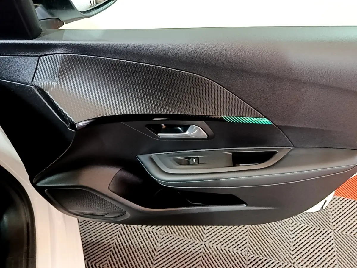 Vue rapprochée de la porte avant gauche blanche d’une Peugeot 208 2021 avec insert décoratif carbone et bouton lève-vitre.