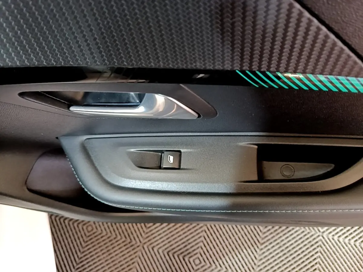 Gros plan sur la commande de lève-vitre et poignée intérieure côté gauche d’une Peugeot 208 blanche, finition Allure Business.