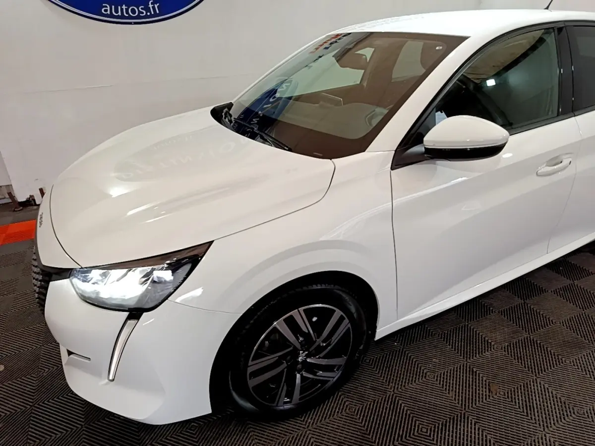 Peugeot 208 blanc vue 3/4 avant droit avec phares LED allumés et jantes alliage noires.