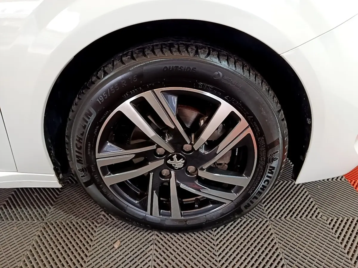 Gros plan sur la roue avant droite d'une Peugeot 208 blanche, jante alliage noire et argent avec logo lion central.