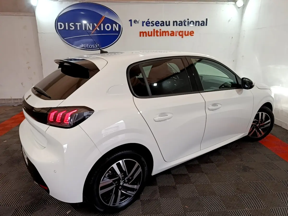 Vue 3/4 arrière droite d'une Peugeot 208 blanche avec feux arrière LED et jantes alliage distinctives.